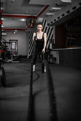 Obraz premium A beautiful girl training with a CrossFit rope in the gym.