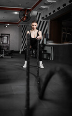 Obraz premium A beautiful girl training with a CrossFit rope in the gym.