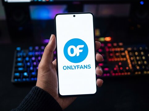 Hand holding a smartphone displaying the OnlyFans mobile application logo on a screen with a vibrant backlit keyboard in the background, representing social media branding and content creator