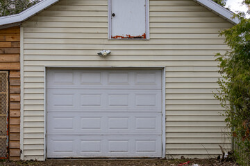 Obraz premium La Tuque, Quebec, 15 May 2026 : A residential building features a white garage door, light yellow siding, and an upper storage door.