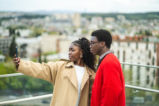 Stylish confident african american man and woman tourists taking selfie on smartphone at local attraction spot in new town, black male and female friends travelers take picture together at camera.