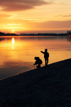 Children silhouettes playing peacefully beside lake during golden sunset evening