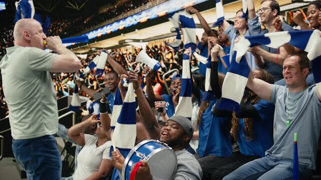 Football chant leader blowing vuvuzela while blue supporters respond from packed stadium stands during energetic live soccer match.