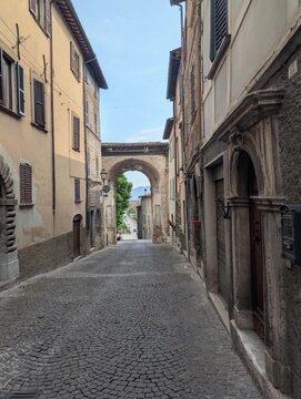 Arco in pietra storico che incornicia la vista sul paesaggio, posto al termine di un vicolo antico con edifici tradizionali. 