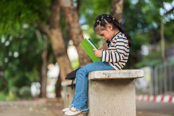 Obraz premium stressed child girl sitting on a concrete bench outdoors of school, reading a book. Education and learning concept.