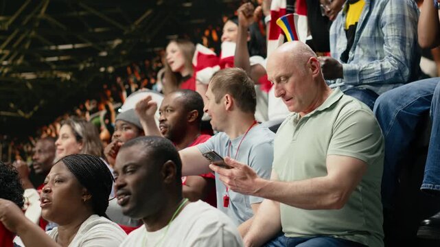 Frustrated football supporter watching tense match moment from stadium stands while crowd behind him cheering with scarves, soccer fan losing online bet ticket, clenched fists and pressure.