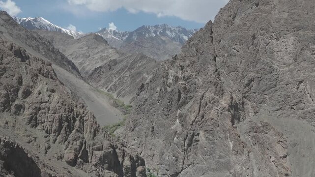 Drone passes between two towering Ladakh peaks flying through the narrow gap into the dramatic valley beyond where layers of rugged rocky ridges unfold ahead and the full scale of the majestic Himalay