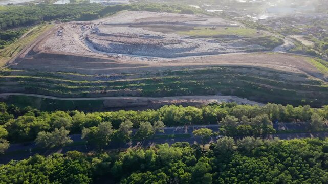 Aerial view of TPA Suwung landfill with massive waste pile near a main road and green forest in Bali