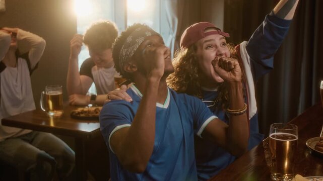 Handheld shot of young diverse sports fans wearing team jersey cheering while watching game in bar and reacting emotionally to sports match result