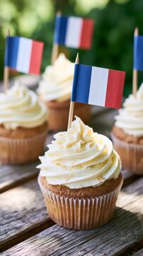 Vanilla cupcakes with French tricolor flags on outdoor wooden picnic table vertical shot