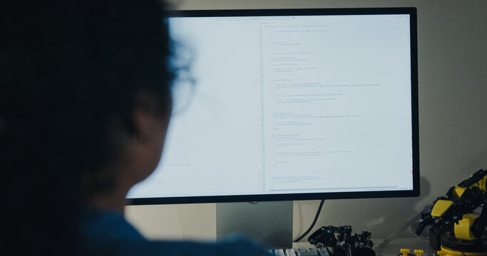 Close-up young Black female programmer coding AI software on multiple screens in night office. Network security, cybersecurity, machine learning, working late, overtime, robotics automation concept.