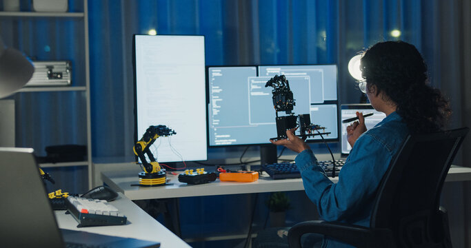 Young African American female programmer coding AI software on multiple screens in night office. Network security, cybersecurity, machine learning, working late, overtime, robotics automation concept.