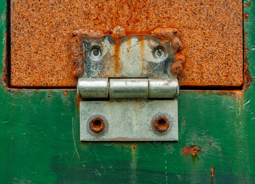A close-up view showcases a rusty metal hinge on an old, green door. The textures convey layers of history and time, illuminated beautifully by the afternoon light.