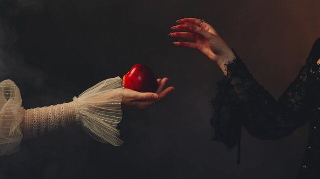 close up body part unrecognizable person fantasy fairy woman holding ripe red apple in hands evil queen hand offers poisoned enchanted apple gift to young beauty princess. Royal black dress two women 