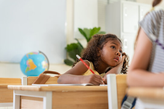 Focused african american girl studying in school classroom, Young student concentrating on writing assignment in classroom, Thoughtful elementary school girl sitting at desk in classroom
