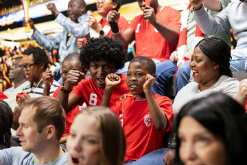 Fototapeta premium Black family cheering together at football stadium during exciting match for home team. Parents supporting their child fan while enjoying family bonding and unforgettable shared experience.