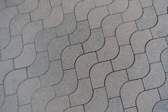 Texture of rounded gray concrete paver blocks with waves like pattern
