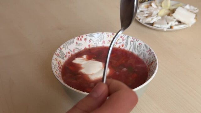 Homemade borscht with sour cream stirred by spoon before eating warm traditional soup