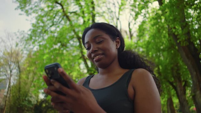 African American woman looking at smartphone and gently shaking head while reading message creating expressive and relatable outdoor lifestyle moment in park environment