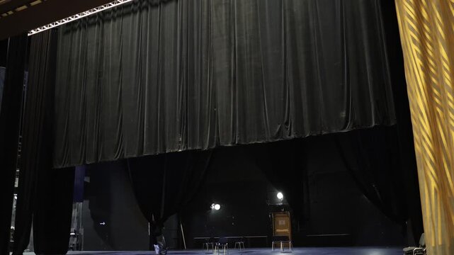 Dark theater stage with closed black curtains empty performance hall and dramatic lighting creating cinematic backstage atmosphere before live show begins