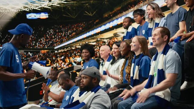 Excited football fan leader using bullhorn to unite blue supporter group in stadium stands during live soccer match atmosphere, passionate football fans in the supporter section singing chants.