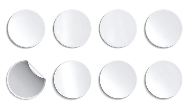 Eight blank white circular stickers with serrated edges and subtle shadows, one sticker peeled back showing a grey underside, isolated on a white background