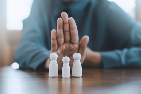 Risk management crisis prevention concept stopping harm, defense, safeguarding, boundary business person hand making stop gesture to protect family wooden peg dolls representing life insurance