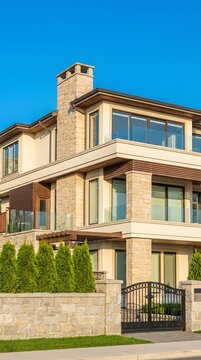 Luxurious Modern Home with Stone Facade and Black Gate Under Clear Blue Sky.