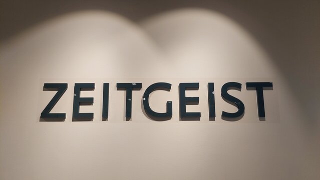 "ZEITGEIST" in schwarzer Schrift auf hellem Hintergrund mit zwei Lichtkegeln