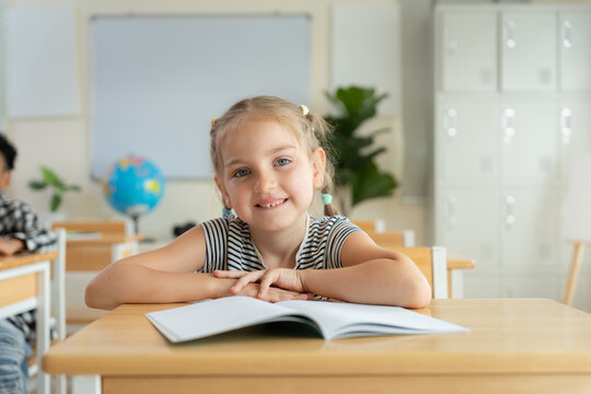 Portrait of a cute primary student studying in school, Smiling young girl sitting at classroom desk with notebook, Happy elementary school girl smiling at desk in classroom