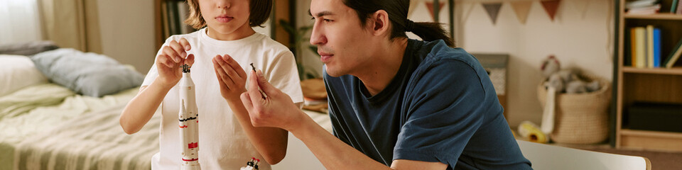 Header of Asian father and child son assembling model rocket together at home, learning engineering...