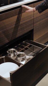 Vertical video. Close-up of woman opening kitchen drawer in modern interior. Stylish storage space and sleek kitchen furniture details with contemporary design. Slow motion 4K video.