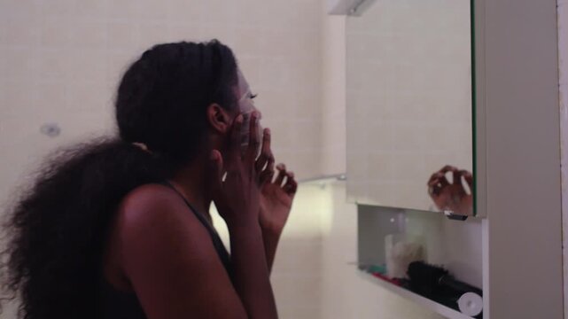 African American woman wearing facial mask in close up as camera pulls back to reveal full bathroom scene, skincare routine expanding from intimate detail to wider personal care environment