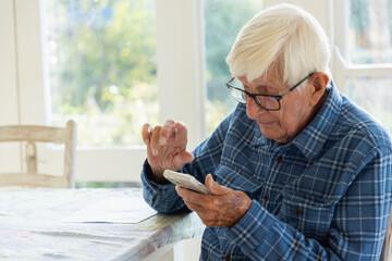 elderly man sitting at table using smart phone
