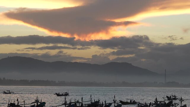 Scenic sunrise over Papuma Beach harbor with silhouettes of traditional fishermen boats floating on misty sea, Jember.
