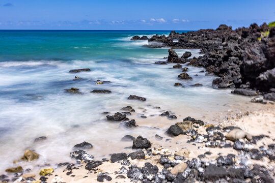 Motion blurred ocean waves washing rocks on beach