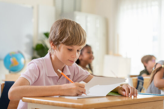 Young boy focused on writing in notebook at school desk, Dedicated student studying and writing assignment in classroom, Caucasian schoolboy doing homework in primary classroom