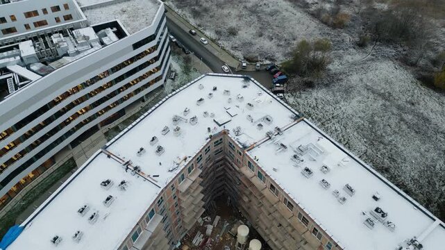 Aerial drone view of a modern residential building under construction in urban area. New apartment complex development with unfinished structure and surrounding cityscape.