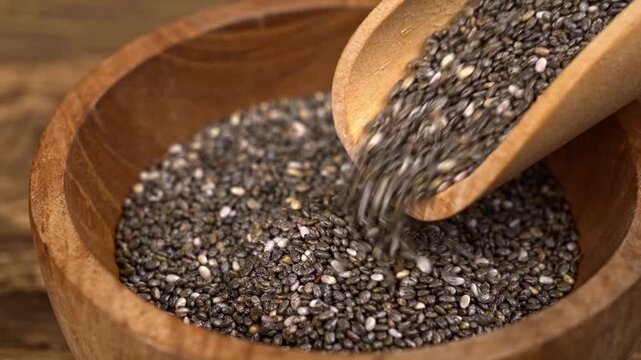Wooden scoop pouring chia seeds into a rustic bowl
