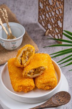 A delicious Indonesian snack called Risol and Risoles filled with chopped vegetables, chicken pieces mayonnaise and fried bread crumbs, served on a white plate on a stone texstured table