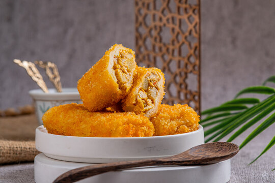 A delicious Indonesian snack called Risol and Risoles filled with chopped vegetables, chicken pieces mayonnaise and fried bread crumbs, served on a white plate on a stone texstured table