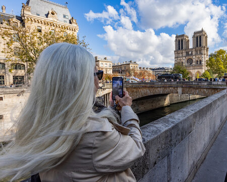Rear view of blonde woman photographing Notre Dame on smart phone