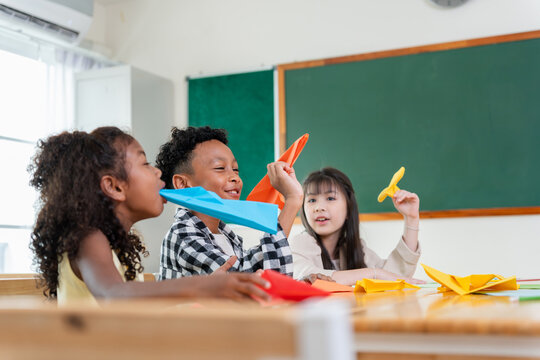 Diverse elementary students playing with paper planes in classroom, Group of happy children having fun with origami at school desk, Creative kids enjoying craft activity and paper planes in classroom