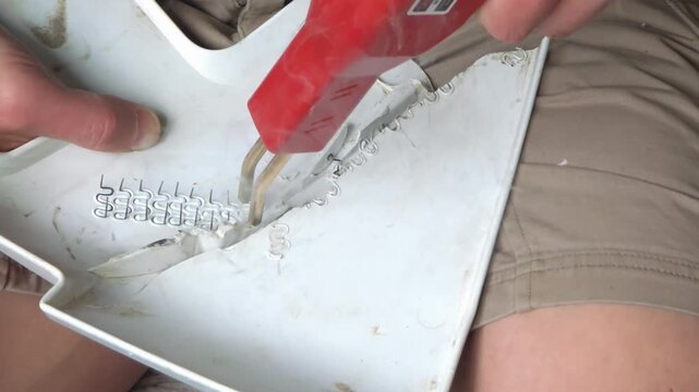 Man repairing plastic part with hot stapler tool. Worker melting metal staple into fractured surface to weld crack. Industrial maintenance for home vehicle fix.