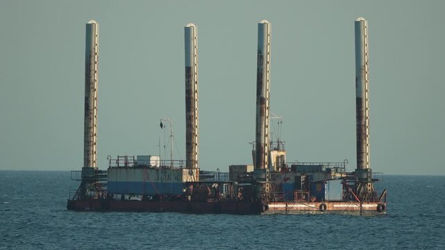 Barge ocean industry, a large industrial vessel with four vertical pillars floats calmly on water under a clear sky, symbolizing offshore work