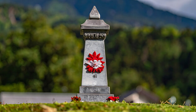 Gravestone adorned with a red and white floral wreath, set against a blurred backdrop of green trees and hills, symbolizing remembrance and memorial