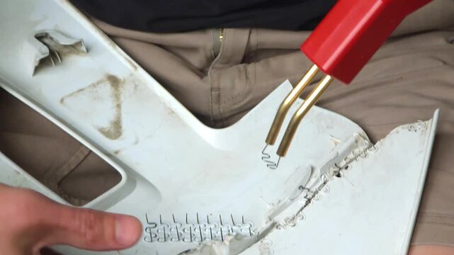 Man repairing broken plastic part with heat welder tool. Technician using hot stapler for bumper crack restoration. Industrial mending process of automotive component.