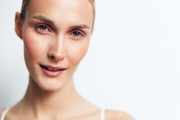 Fototapeta premium Young woman with clear skin and light makeup smiles gently in a close-up portrait against a white background conveying natural beauty and confidence.