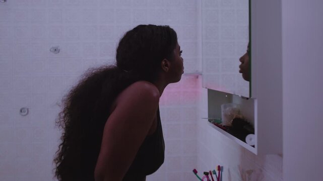 African American woman leaning toward mirror as camera moves closer, reflecting on personal doubts, searching for clarity, resilience, and self acceptance during quiet moment of introspection