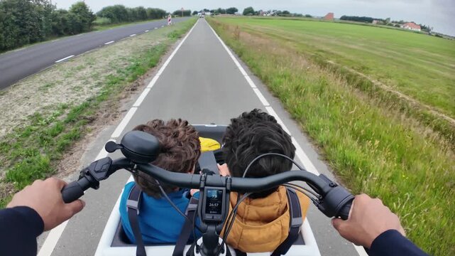Father riding an electric cargo bike with two kids on a dedicated cycling path in the countryside, a first-person perspective showing a sustainable family commute